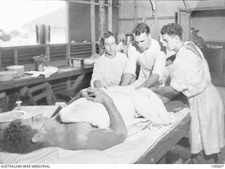 Lae, New Guinea. 1944-08-02. Lieutenant J. Growse, Physiotherapist (1), assisting Major E. A. Hedberg, Medical Officer (2), and an orderly in the plaster room at 2/7th Australian General Hospital