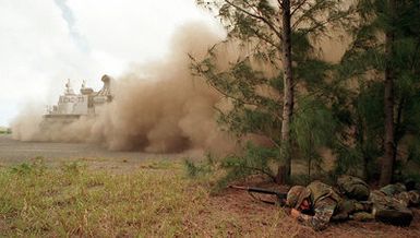 US Marine Lance Corporal (LCPL) Walter Embser armed with 5.56mm M16a2 assault rifle covers his face from a barrage of dust and debris stirred up by The US Navy Landing Craft Air Cushion (LCAC 73) departing from Kaneohe Bay Marine Corps Station, HI. Marine and Naval Personnel from conducted simulated Noncombatant Evacuation Exercises as part of Operation RIMPAC 96