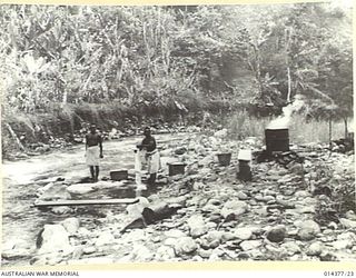 1943-03-03. WASHING DAY AT WAU. A PEACEFUL DOMESTIC SCENE SHOWING NATIVE SERVANTS WITH THEIR COPPER SET UP BY ONE OF THE CREEKS THAT TUMBLE INTO THE BULOLO RIVER, DOING SOME WASHING FOR THE ARMY. ..