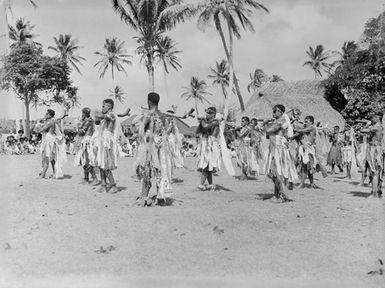 [Pacific island men with Fijian style staffs engaging in a village ceremony]