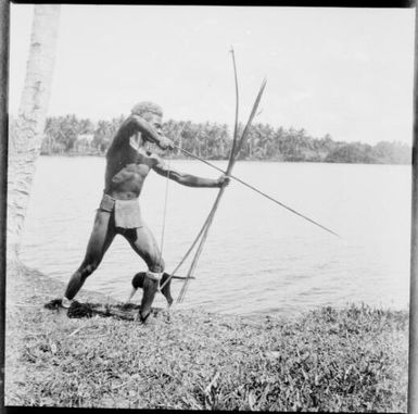 Ramu man aiming bow and arrow into river with a dog at his feet, Ramu River [?], New Guinea, 1935 / Sarah Chinnery