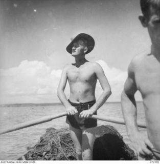 YULE ISLAND, NEW GUINEA. 1944-05-20/11. PRIVATE HARGREAVES, 1ST MARINE FOOD SUPPLY PLATOON (1), SCANNING THE WATER FROM THE DINGHY FOR A LIKELY SPOT TO TRAWL THE NET