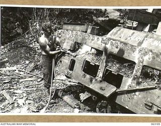 FINSCHHAFEN AREA, NEW GUINEA.  NX140713 STAFF SERGEANT J. E. SAUNDERS OF THE 1ST TANK GROUP BATTALION WORKSHOPS USING AN OXYACETYLENE CUTTING TORCH WHILE CANNIBALISING A DAMAGED TANK FOR PARTS.  ..