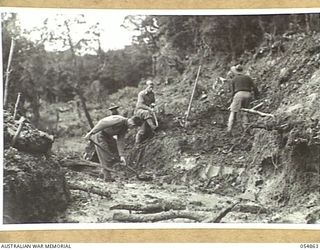 BULLDOG-WAU ROAD, NEW GUINEA, 1943-07-20. TROOPS OF THE 9TH AUSTRALIAN FIELD COMPANY, SHIFTING SOIL NEAR JOHNSON'S GAP WITH PICK AND SHOVEL