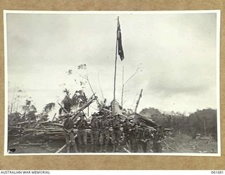 WAREO, NEW GUINEA. 1943-12. OFFICERS OF THE 2/23RD AUSTRALIAN INFANTRY BATTALION, GROUPED AROUND THE VICTORY FLAG. THIS FLAG WAS PREVIOUSLY RAISED OVER KOKODA, BUNA AND SATTELBERG. VX50364 CAPTAIN ..