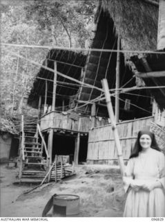 Ramale Mission, Kokopo Area, New Britain. An unidentified nun stands in front of the sleeping quarters of the nuns at Ramale Mission, built native style. A group of 300 white internees at the ..