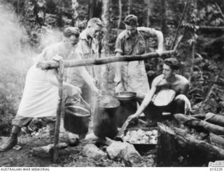 NEW GUINEA. WAU-MUBO AREA. COOKS AT A FORWARD CAMP PREPARE A MEAL FOR TROOPS PASSING THROUGH TO THEIR BATTLE STATIONS, ON THE MUBO TRACK. LEFT TO RIGHT PTES. K. LEWIS, OF ST KILDA, VICTORIA, J. ..