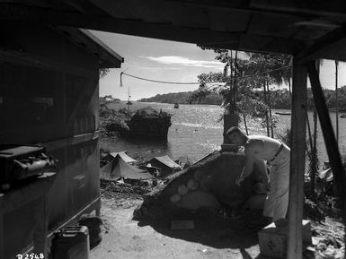 Soldier next to [a makeshift oven?] in an army camp on Mono Island, Solomon Islands