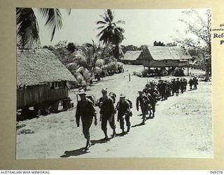 MENDAROPU, NEW GUINEA. 1942-11. INFANTRYMEN OF THE 128TH REGIMENT, 32ND UNITED STATES DIVISION MOVING ALONG THE TRACK PAST A FORMER MISSION STATION ON THE GRASSY HEIGHTS OVERLOOKING DYKE ACLAND BAY