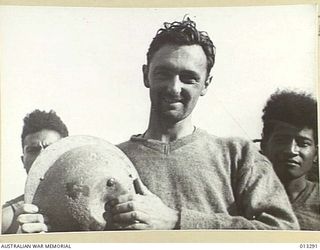 VX13966 Lieutenant Ian McLeod Hutchison, 2/14 Australian Infantry Battalion of Elwood, Vic, displays his tin hat which was dented by a spent Japanese bullet