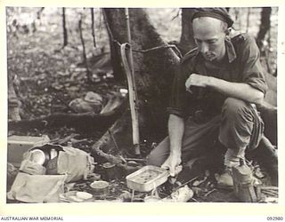 BOUGAINVILLE. 1945-05-31. SIGNALMAN B.A. RUTHENBERG, 47 INFANTRY BATTALION, 29 INFANTRY BRIGADE, BOILING A DIXIE OF WATER OVER CANNED HEAT WHEN A FIGHTING PATROL, ASSISTED BY NATIVES OF AUSTRALIAN ..