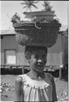 Smiling older woman with basket of food and bowls carried on her head