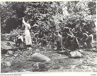 1943-08-10. NEW GUINEA. MOUNT TAMBU FIGHTING. WITHIN SOUND OF RIFLE, ARTILLERY AND MORTAR FIRE, FATHER THEO O'KEEFE, OF ST PATRICK'S CHURCH, CAMPERDOWN, VIC., HOLDS MASS ALONGSIDE A MOUNTAIN STREAM ..