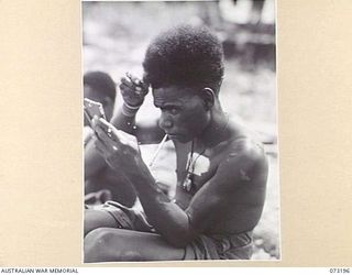 ALEXISHAFEN, NEW GUINEA. 1944-05-14. JEROL (1), A SIO NATIVE, TRIMMING HIS HAIR WITH A RAZOR BLADE