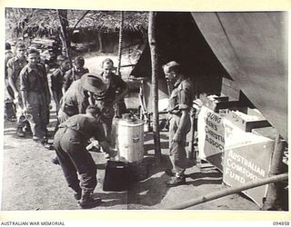 YAMIL SECTOR, NEW GUINEA, 1945-08-01. TROOPS OF 2/6 INFANTRY BATTALION IN LINE FOR THEIR MUG OF COFFEE OR TEA AT THE YMCA CENTRE. MR A.K. HILLIS, YMCA OFFICER IS SEEN POURING IT OUT FOR THE TROOPS