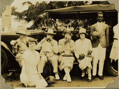 Group drinking coconut milk on the running board of a car, 1928