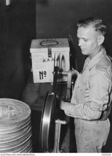 NEW GUINEA. 1944-01-08. SERGEANT H. H. SHIERS OF ADELAIDE, SA, IS IN CHARGE OF RAAF WELFARE ACTIVITIES AT A NEW GUINEA STATION. HERE HE IS REWINDING FILM FOR A CINEMA SHOW