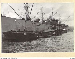 WEWAK BEACH, NEW GUINEA. 1945-10-18. A BARGE TIED UP BESIDE THE CARGO SHIP WITH THE SLINGS OF THE SHIP SWINGING STORES OVER THE SIDE. THE UNLOADING OPERATIONS ARE BEING HANDLED BY 8 PORT OPERATING ..