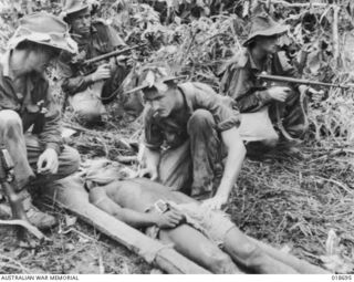 VX501799 (VX9453) Sergeant John Henry Daniel of Holbrook, NSW (2nd from left in background), carried this wounded native boy (on stretcher) to a safe place while under fire from enemy snipers. He ..