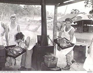 RABAUL, NEW BRITAIN, 1945-12-25. CORPORAL R. E. WHITEHEAD (1) AND PRIVATE F. M. POWELL (2) TAKING THE TURKEYS FROM THE OVENS IN A COMPANY KITCHEN WHILE COOKING CHRISTMAS DINNER AT HEADQUARTERS ..