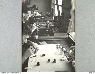 PORT MORESBY, NEW GUINEA. 1944-04-10. VX138279 CRAFTSMAN O.B. BUTCHER, WITH VX138278 CRAFTSMAN A.F. SUTHERLAND, AND QX50160 CRAFTSMAN R.J. BRADLEY, WORKING IN THE WATCH REPAIR SECTION AT THE 11TH ..