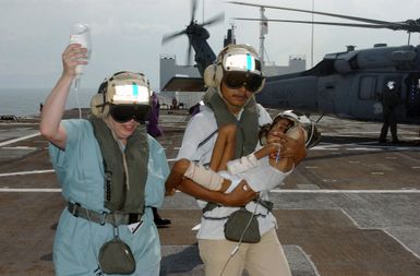 A Nurse from Project HOPE (a civilian organization of medical volunteers) carries an IV bag and guides an Indonesian man carrying his boy away from a US Navy (USN) MH-60S Seahawk helicopter, Helicopter Combat Support Squadron 5 (HC-5), Andersen Air Force Base (AFB), Guam, aboard the Military Sealift Command (MSC) Hospital Ship USNS MERCY (T-AH 19). The boy was airlift to the MERCY for treatment. The MERCY is currently off the waters of Indonesia in support of Operation UNIFIED ASSISTANCE the humanitarian relief effort to aid the victims of the Tsunami that struck Southeast Asia on December 26, 2004