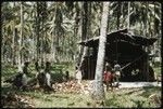 People around a pile of coconut halves next to a building