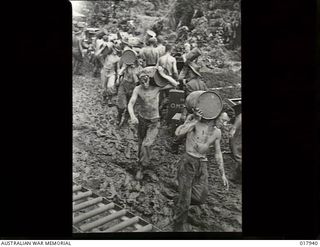 Jacquinot Bay, New Britain. 1945. Australian infantrymen walking through mud and slush carrying drums of flour and sugar to a supply dump in the area