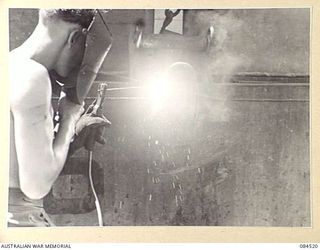 LABU, NEW GUINEA. 1944-12-18. SAPPER W.F. THOMAS CARRYING OUT REPAIRS TO THE STERN OF AN AUSTRALIAN LANDING CRAFT AT 55 PORT CRAFT COMPANY WITH AN ELECTRIC WELDING TORCH