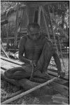 Canoe-building: man, Tovalugwa, smoothes thin pole, using an axe with traditional handle