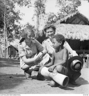 NEW GUINEA. 1943-11-17. MEMBERS OF THE AUSTRALIAN ARMY MEDICAL WOMEN'S SERVICE (AAMWS), BETTY COOK OF ADELAIDE, SA, AND PAM BUSHELL, OF DARLING POINT, N.S.W., WATCH YOUTHFUL LOCAL BOY, VAKARAI, AS ..