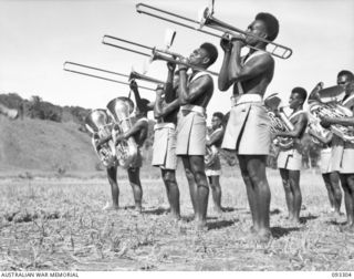 NADZAB AREA, NEW GUINEA, 1945-06-27. THE DEPOT BAND, PACIFIC ISLANDS REGIMENT, PLAYING DURING THE VISIT OF HIS ROYAL HIGHNESS, THE DUKE OF GLOUCESTER, GOVERNOR GENERAL OF AUSTRALIA. THE GOVERNOR ..