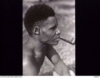 BUKAUA, NEW GUINEA. 1943-10-18. PORTRAIT OF MAGASI WITH A PIPE IN HIS MOUTH, A VOLUNTEER FOR THE AUSTRALIAN AND NEW GUINEA ADMINISTRATION UNIT LABOUR FORCE