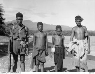 HOPOI, NEW GUINEA, 1943-10-20. YAMBO (LEFT) A NATIVE CONSTABLE WITH SOME NEW ACQUAINTANCES, NATIVE VILLAGERS FROM THE HOPOI AND BUKAUA VILLAGES ON THE BEACH