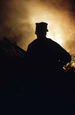 PH1 Ted Salois Tinian, Marianas Islands....A Marine is silhouetted by a burning flare as he moves toward a Seabee camp during exercise Kennel Bear '89. Marines from Marine Barracks Guam are acting as aggressors against Seabees from Navy Mobile Construction Battalion 3 and Marines from the 3rd Force Service Support Group. OFFICIAL U.S. NAVY PHOTO (RELEASED)