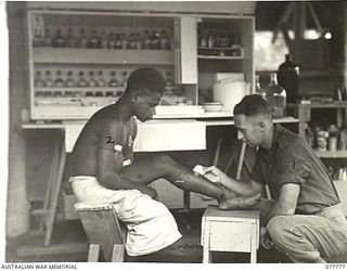 LAE BASE AREA, NEW GUINEA. 1944-12-29. NX102350 LANCE CORPORAL H.J. NORTON, MEDICAL ORDERLY (1) TREATING THE LEG OF TIPAN (2) A NATIVE BOY EMPLOYED BY THE UNIT, IN THE REGIMENTAL AID POST OF THE 1 ..