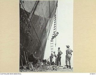 1943-09-25. NEW GUINEA. FALL OF LAE. SOLDIERS BESIDE THE HULL OF THE WRECKED JAPANESE SHIP MYOKO MARU AGROUND ON A BEACH NEAR LAE