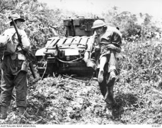 Sattelberg, New Guinea. 1943-11-16. Australian troops moved in behind Matilda tanks for a dawn attack on the Japanese held village of Sattelberg. A wounded soldier is carried back from the forward ..