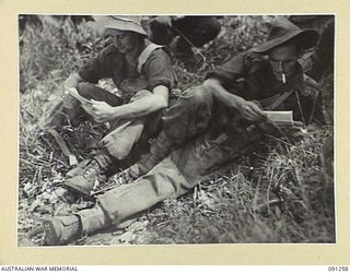 KALIMBOA, AITAPE-WEWAK SECTOR, NEW GUINEA. 1945-04-26. GNR F.S. SYKES (1) AND CAPT P.G. TATCHELL (2), MEMBERS OF 2/3 INFANTRY BATTALION READING MAIL IN THE FRONT LINE