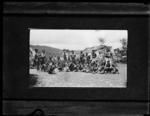 Group of approximately 40 people standing in front of village dwellings.