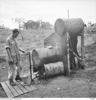 ORO BAY, NEW GUINEA. 1943-07. PRIVATE A. GADSDEN DRAWING HOT WATER FROM THE IMPROVISED WARD HOT WATER SYSTEM AT THE 10TH FIELD AMBULANCE