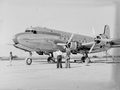 [Three men standing before a 'Pacific Overseas Airlines' plane]