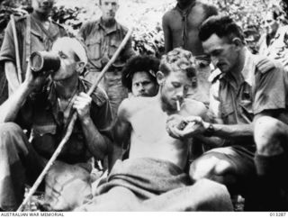 A wounded Australian soldier has his cigarette lit by Salvation Army Chaplain Albert Moore, padre to the 2/14th Battalion. The soldier on the stretcher is VX51106 Lieutenant Valentine G. Gardner, D ..