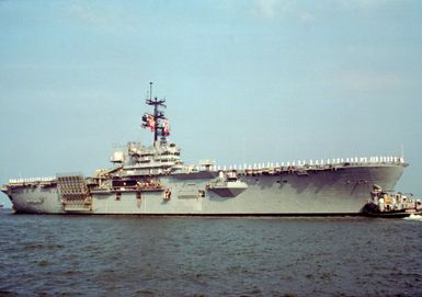 The large harbor tug WATHENA (YTB-825) maneuvers the amphibious assault ship USS GUAM (LPH-9) while sailors man the rail as the vessel departs for the Persian Gulf in support of Operation Desert Shield