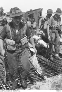 AITAPE BEACH, NEW GUINEA. 1944-11-26. CORPORAL M. GILL, SECTION LEADER, D COMPANY, 2/7 INFANTRY BATTALION (1), MOVING ASHORE FROM A LANDING BARGE