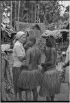 Mortuary ceremony, Omarakana: mourning woman with shaved head and wearing necklace carries banana leaf bundles for exchange, talks with anthropologist Annette Weiner