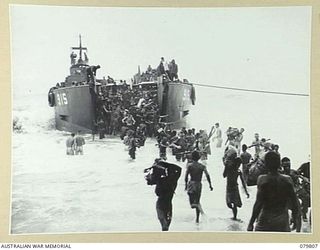 TOKO, BOUGAINVILLE, SOLOMON ISLANDS. 1945-03-20. 4TH BATTERY, 2ND FIELD REGIMENT PERSONNEL ASSISTED BY NATIVES UNLOAD THEIR GEAR FROM THE LST (LANDING SHIP, TANK) AFTER THEIR ARRIVAL FROM MAWARAKA