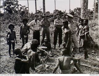 Kirawina Island, New Guinea, 1945-02. Officers from Headquarters, RAAF Northern Command (NORCOM), watch as Kirawina natives trade wooden carvings