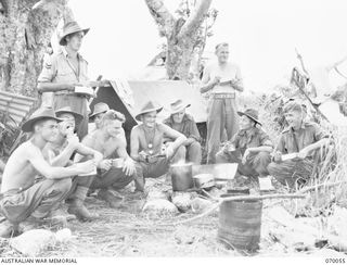 SIO MISSION, NEW GUINEA. 1944-01-24. LUNCH TIME NEAR THE 23RD BATTERY OBSERVATION POST, 2/12 FIELD REGIMENT. GUNNERS AND OFFICERS EATING ROUND THE FIRE. IDENTIFIED PERSONNEL ARE: QX55796 GUNNER J. ..