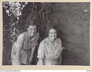 LAE, NEW GUINEA, 1945-05-18. SERGEANT J. GRIEVE (1), AND SERGEANT E.M. JONES (2), PERSONNEL FROM AUSTRALIAN WOMEN'S ARMY SERVICE BARRACKS, LOOKING DOWN THE ENTRANCE OF A JAPANESE FOXHOLE. THEY ARE ..